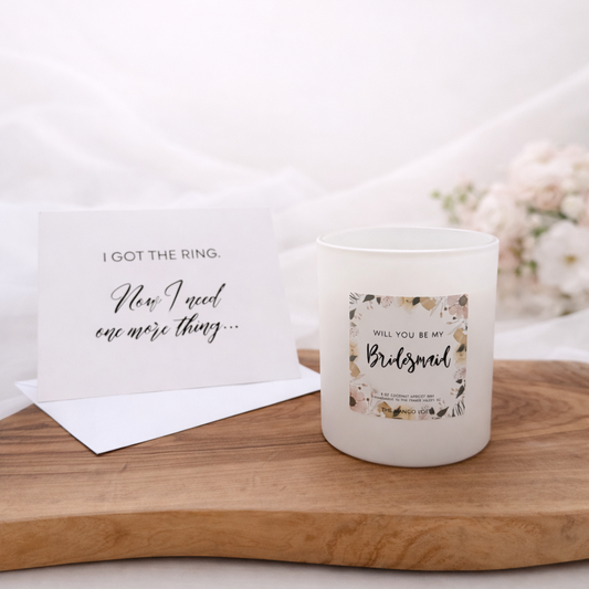 Candle with 'Will you be my bridesmaid?' message on a wooden board with a card in the background.